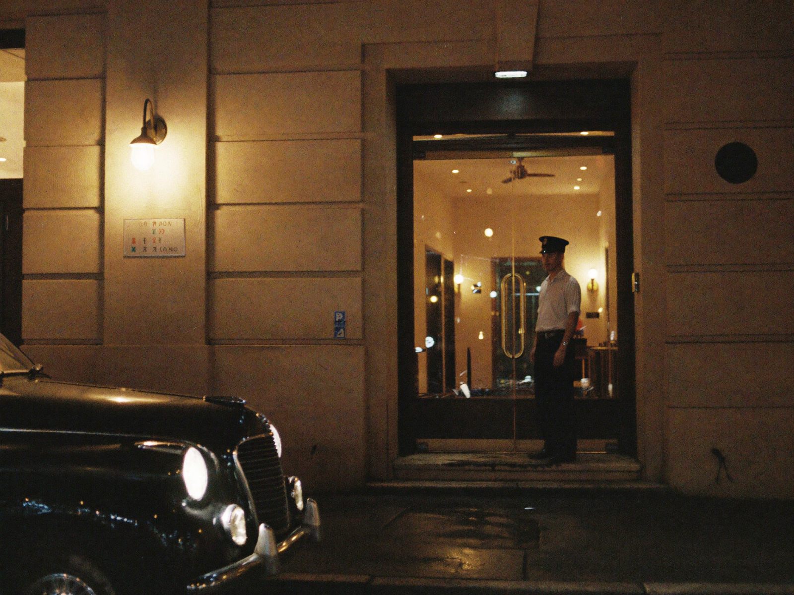 La entrada del Salón Aurora de noche, con su portero y un auto antiguo